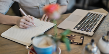 a business professionals desk with a person's hand writing in a journal